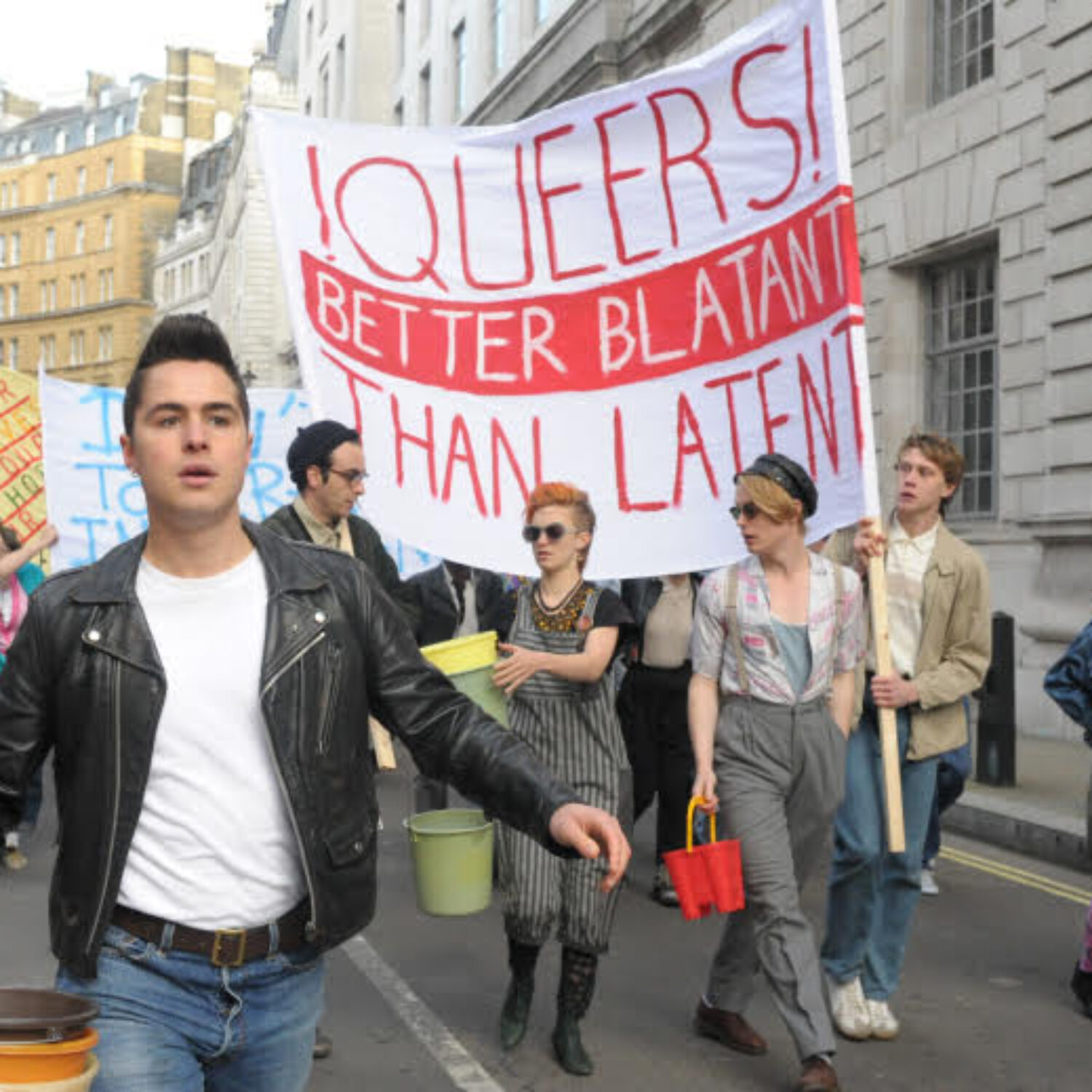 Eine Demonstration in der Innenstadt. Ein Banner mit der Aufschrift "!QUEERS! Better blatant than latent" wird von jungen Menschen hochgehalten.